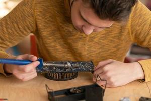 un joven suelda un microcircuito quemado con un soldador foto