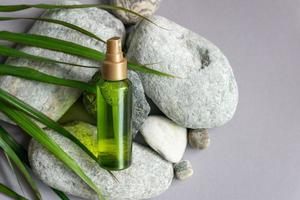 A bottle of green color with a spray bottle lies on the stones, next to the green leaves and berries of schisandra chinensis photo