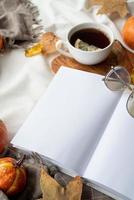 white blank book with autumn leaves and cup of hot tea on table , book mockup design photo