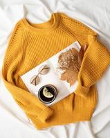 cozy composition of warm sweater, white book , cup of hot tea and autumn leaves , top view photo