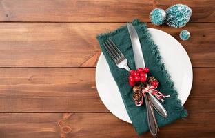 Christmas table setting with white dishware, silverware and green decorations on wooden background. Top view. photo