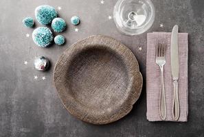Christmas table setting with black dishware, silverware and green decorations on dark background. Top view. photo