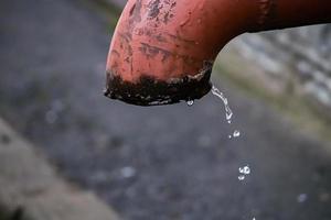 Water droplets flow from old rusty pipe. Water scarcity on planet. Concept of land pollution and fossil sources problem. photo