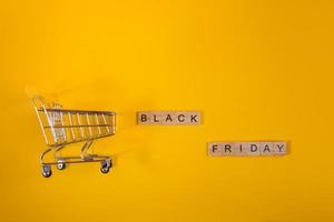 venta y concepto de viernes negro. mini carrito de compras sobre fondo amarillo. foto