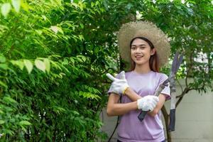 asian Woman wear hat pruning bushes with big garden scissors. photo