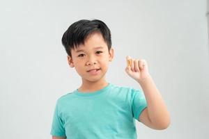 Smiling boy holding a capsule of vitamin on a white background photo