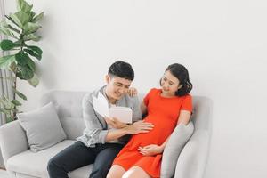 Asian pregnant woman and husband sitting on sofa and reading book photo