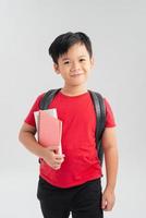 Smiling cute schoolboy with backpack holding books and looking at camera isolated on white background photo