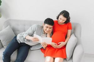 marido leyendo un libro para su esposa embarazada en el sofá de casa foto