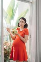 Pregnant woman in livingroom eating a salad smiling photo