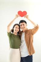 Beautiful young loving couple is holding a card in the shape of heart over white background. photo