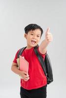 Happy schoolboy wearing backpack and giving thumbs up isolated on white photo