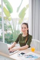 woman sitting at the table at home working using computer laptop with a happy face standing and smiling with a confident smile showing teeth photo