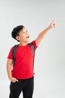 hermoso niño estudiante con mochila sosteniendo un libro sobre un fondo blanco aislado muy feliz señalando con la mano y el dedo al lado foto