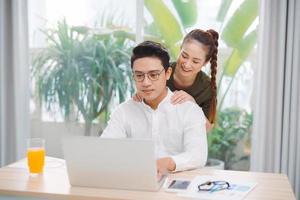 Joyful beauty couple spending time at home. Bright spacious apartment, cookies and drinks and watching laptop with surprise photo