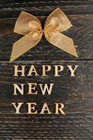 happy new year greeting text on wooden background with scattered golden confetti and tied bow. Festive card for design with copy space photo