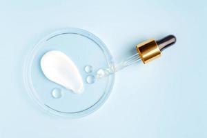 smear of cream stroke and round transparent drop of gel serum in a petri dish on a blue background. Concept laboratory tests and research, making and testing cosmetic photo