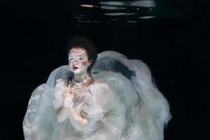 mujer joven en vestido largo de lujo blanco bajo el agua en el fondo negro. movimiento, arte, concepto de invierno foto