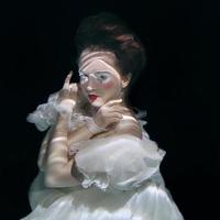 young woman in long white luxury dress underwater on the black background. Motion, art, winter concept photo