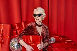 mujer elegante senior con regalos sobre fondo rojo. fiesta, moda, celebración, concepto anti edad. foto