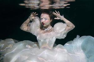 mujer joven en vestido largo de lujo blanco bajo el agua en el fondo negro. movimiento, arte, concepto de invierno foto