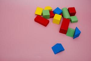 Colorful wooden blocks on pink background. Creativity toys. Children's building blocks. Geometric shapes - cube, triangular prism, cylinder. The concept of logical thinking. photo