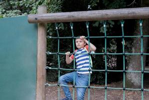 Portrait Kid holding robe in outdoors playground, Child climbing adventure park on sunny day  Spring or sSmmer, Lonely young boy playing alone in public playground. photo