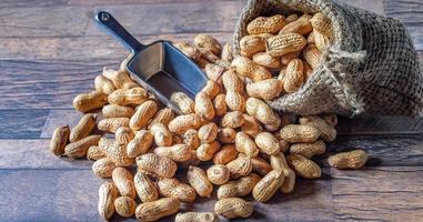 cacahuetes secos o nueces en sacos marrones vertidos sobre fondo de madera foto