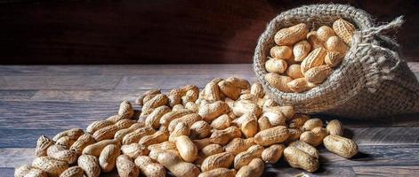 cacahuetes secos o nueces en sacos marrones vertidos sobre fondo de madera foto