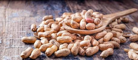 cacahuetes secos o nueces sobre fondo de madera. cáscaras de maní en una cuchara de madera foto