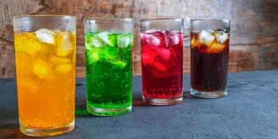 un montón de refrescos en vasos coloridos y sabrosos sobre la mesa,vasos con bebidas dulces con cubitos de hielov foto