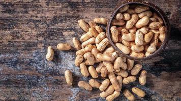 cacahuetes secos o nueces sobre fondo de madera. cáscaras de maní en una cuchara de madera foto