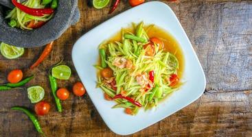 Thai food papaya salad on a plate with lemon and tomato on a wooden background.Top view photo