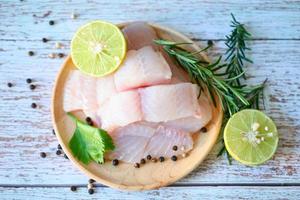 fresh raw pangasius fish fillet with herb and spices black pepper lemon lime and rosemary, meat dolly fish tilapia striped catfish, fish fillet on wooden plate with ingredients for cooking photo
