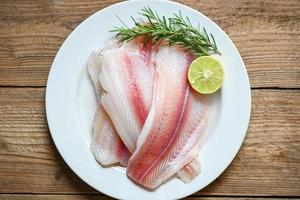 fresh raw pangasius fish fillet with herb and spices lemon lime and rosemary, meat dolly fish tilapia striped catfish, fish fillet on white plate with ingredients for cooking photo