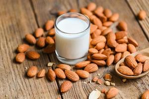 leche de almendras y nueces de almendras fondo de madera, deliciosas almendras dulces en la mesa, nueces de almendras tostadas para comida saludable y bocadillos foto