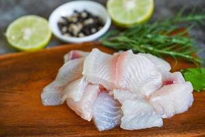 filete de pescado pangasius crudo fresco con carne, pescado dolly, bagre rayado tilapia, filete de pescado sobre tabla de madera con ingredientes apio para cocinar foto