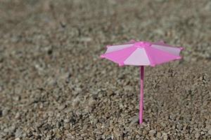 Toy umbrella in pink and white colors on the beach, by the sea. Selective focus. photo