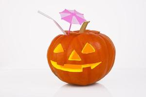 Orange pumpkin with glowing eyes, nose and mouth, cocktail pipe and cocktail umbrella, sunshade on a white background. halloween photo
