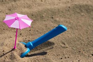 Children's sandbox, a toy pink umbrella and a blue shovel on a sandy beach. Vacation with children. Children's psychedelic photo