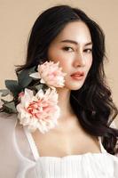 Asian woman with a beautiful face and Perfect clean fresh skin with flower. Cute female model with natural makeup and sparkling eyes on beige isolated background. photo