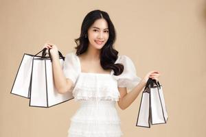 joven mujer asiática de moda sosteniendo bolsas de compras aisladas en fondo beige y copiando espacio. pago de compras en línea. foto