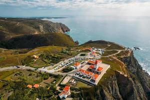 Aerial drone view of lighthouse at Cabo da Roca with unidentifiable tourists enjoying the amazing views. Guincho Beach is visible in the far background photo