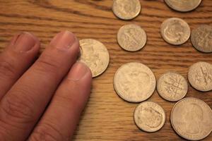 mano recogiendo un cuarto de moneda en moneda americana esparcida en el suelo de madera foto