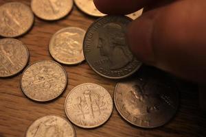 mano recogiendo un cuarto de moneda en moneda americana esparcida en el suelo de madera foto