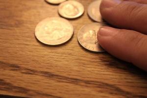 mano recogiendo un cuarto de moneda en moneda americana esparcida en el suelo de madera foto