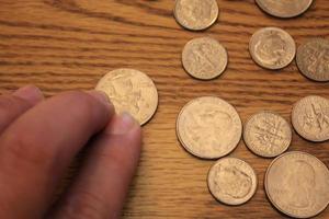 mano recogiendo un cuarto de moneda en moneda americana esparcida en el suelo de madera foto