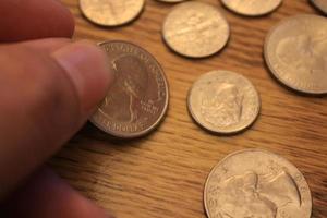 mano recogiendo un cuarto de moneda en moneda americana esparcida en el suelo de madera foto