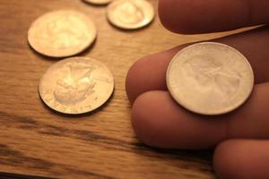 mano recogiendo un cuarto de moneda en moneda americana esparcida en el suelo de madera foto