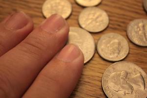 mano recogiendo un cuarto de moneda en moneda americana esparcida en el suelo de madera foto